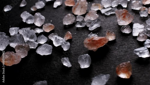Close-up of Himalayan pink SALT crystals on a black surface. Macro view of coarse, irregular grains used in cooking and wellness products.