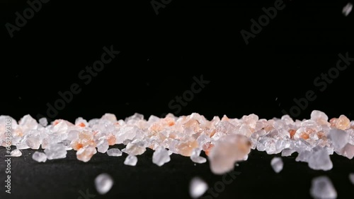Himalayan SALT crystals fall and bounce across a black surface in slow motion. Close-up shows structure, clarity and variety of natural grains.