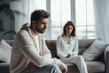 In a couple's emotional turmoil, a despondent man sits on the sofa, his partner's sadness palpable, reflecting relationship tension and an impending breakup