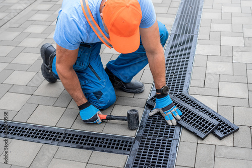 Laying interlocking paving. A worker's hand is placing drainage channel on an area made of interlocking paving. photo