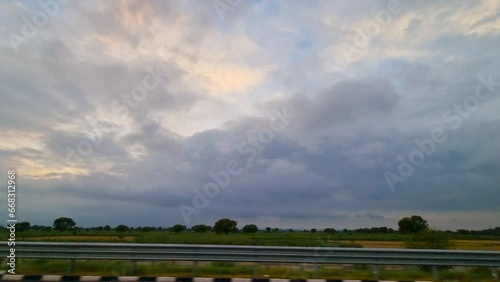 side view of road trip with signs rushing past, fluffy monsoon clouds at dusk and sunset colors in the distance showing the beauty of long drives in India photo