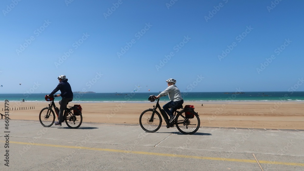 Cyclisme / cyclotourisme à Saint-Malo en Bretagne, deux cyclistes séniors faisant du vélo sur une digue au bord de la mer (France)