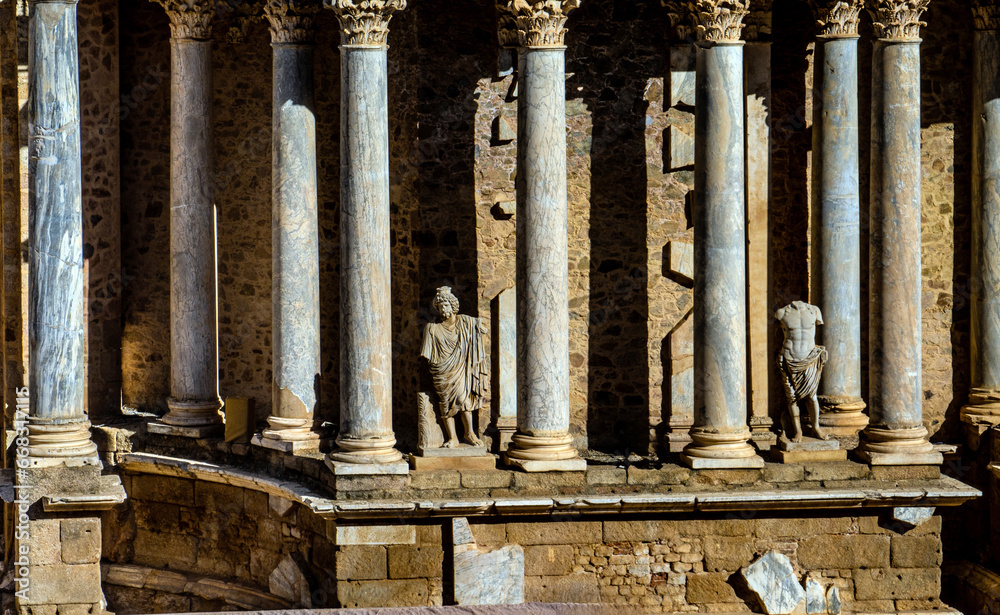 Classic statues without heads and Greek and Roman columns from the Roman Theater of Mérida in Extremadura, illuminated by the contrasting light of dawn creating shadows on the granite wall. Classic statues without heads and Greek and Roman columns from the Roman Theater of Mérida in Extremadura, illuminated by the contrasting light of dawn creating shadows on the granite wall.