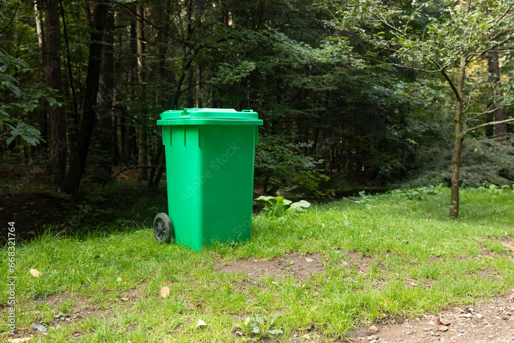 green plastic trash can in a forest park. green plastic trash can in a forest park.