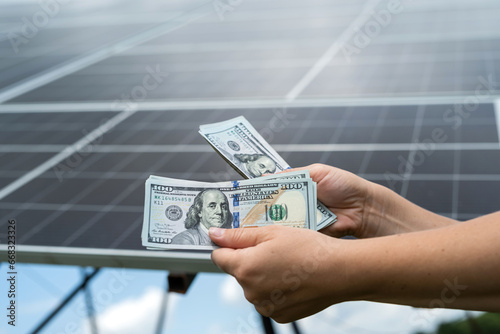male hand hold hundred dollar against solar station, saving concept