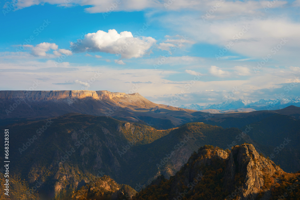 Fototapeta premium Picturesque mountain landscape with a rocky snow-capped ridge in the distance under a beautiful cloudy sky before sunset.