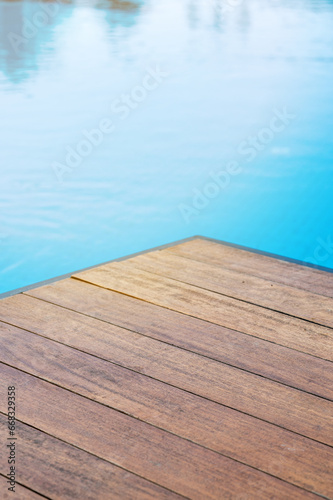 Empty wooden tabletop in front of a swimming pool with blue tiles. Concept for product presentation display with summer background.