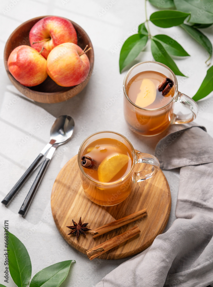 Homemade apple cider with apples and cinnamon in glasses on a light background with fresh fruits, spices and branch. The concept of an autumn or winter healthy drink. Homemade apple cider with apples and cinnamon in glasses on a light background with fresh fruits, spices and branch. The concept of an autumn or winter healthy drink.
