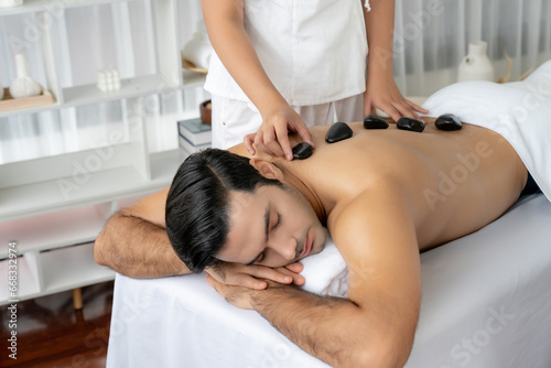 Hot stone massage at spa salon in luxury resort with day light serenity ambient  blissful man customer enjoying spa basalt stone massage glide over body with soothing warmth. Quiescent