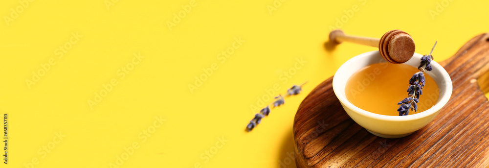 Bowl of sweet lavender honey and dipper on yellow background with space for text