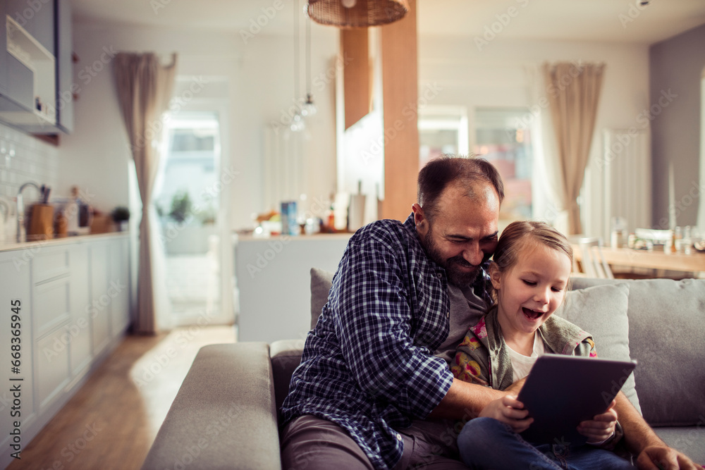Young Caucasian father and daughter using a tablet on the couch at home Young Caucasian father and daughter using a tablet on the couch at home