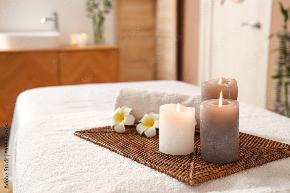 Burning candles with flowers and towel on couch in spa salon, closeup