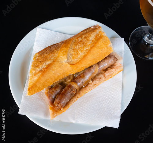 In fast food restaurant, appetizer of their fresh baguette with juicy pork sausages and fried onions is served with glass of cold beer