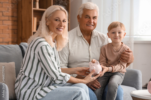 Little boy with his grandparents putting coin in piggy bank at home © Pixel-Shot