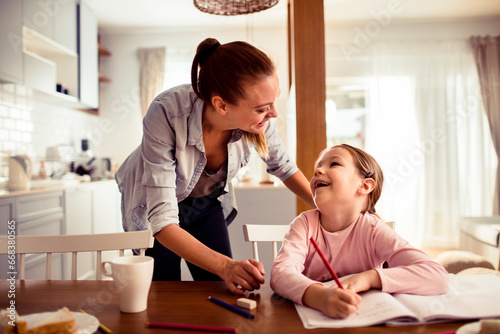 Loving young mother helping her daughter with homework at home