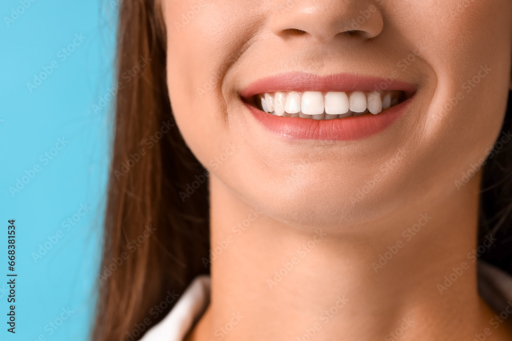Fototapeta premium Smiling young woman with healthy teeth on blue background, closeup