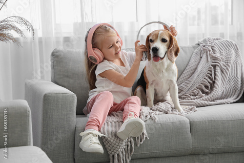 Cute little girl in headphones with Beagle dog at home