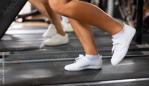 Feet of woman in sneakers training on treadmill in gym close-up