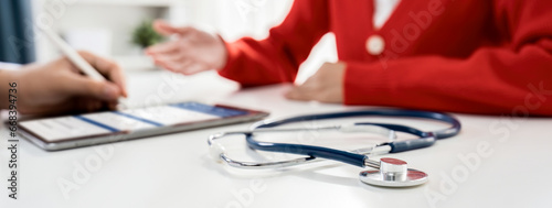 Focused stethoscope on office desk with blurred background of patient attending to doctor appointment at clinic or hospital discussing medical treatment or examining symptoms. Panorama Rigid photo