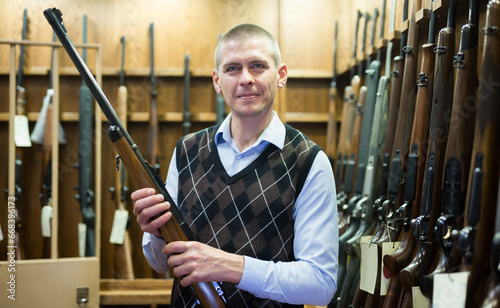 Portrait of male customer which is choosing combat rifle gun in army market.