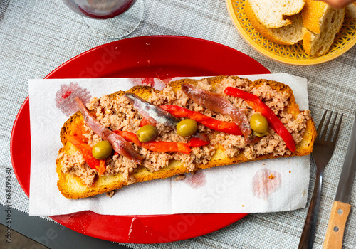 Crispy toast with tuna green olives, red sweet pepper slices and anchovy .