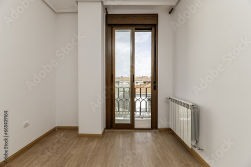 empty room with white painted walls and light wooden floors and access to a balcony with sliding aluminum and glass doors