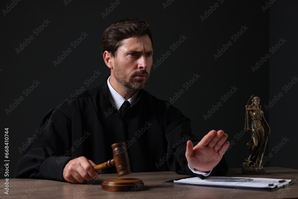 Judge with gavel and papers sitting at wooden table against black background Judge with gavel and papers sitting at wooden table against black background