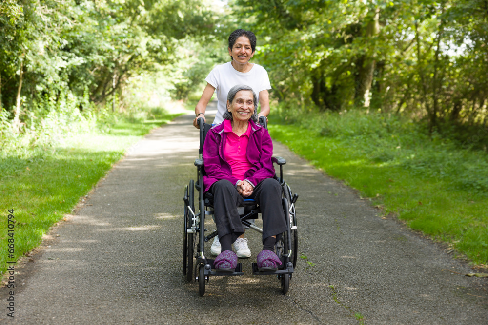 Elderly Indian woman outdoors in a wheelchair with carer, UK Elderly Indian woman outdoors in a wheelchair with carer, UK