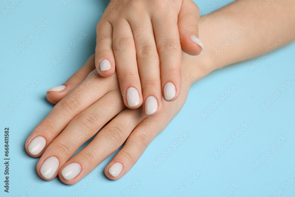 Woman showing her manicured hands with white nail polish on light blue background, closeup Woman showing her manicured hands with white nail polish on light blue background, closeup
