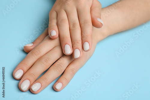 Woman showing her manicured hands with white nail polish on light blue background  closeup