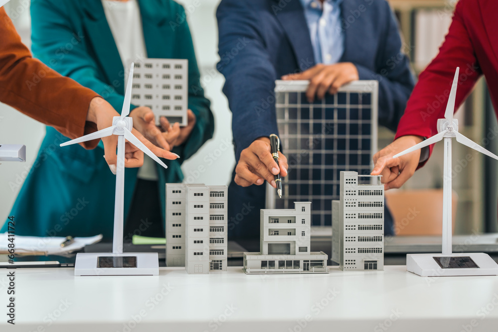 Four asian businesspeople professionals discuss renewable energy in office, showing solar panel and wind turbines with tower building model, apartment. modern business with environmental, clean energy Four asian businesspeople professionals discuss renewable energy in office, showing solar panel and wind turbines with tower building model, apartment. modern business with environmental, clean energy