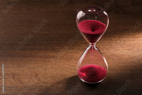 Hourglass with pink flowing sand on wooden table. Space for text