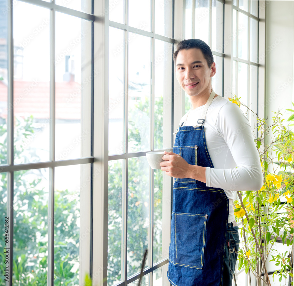 Gardener adult young Asian man one person handsome cool standing think look and Smile relax happy drinking a cup of coffee in the room cafe with glass window and green trees in spring morning time. Gardener adult young Asian man one person handsome cool standing think look and Smile relax happy drinking a cup of coffee in the room cafe with glass window and green trees in spring morning time.