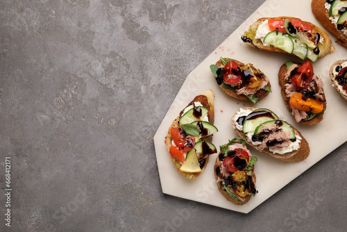 Delicious bruschettas with balsamic vinegar and different toppings on grey textured table, top view. Space for text