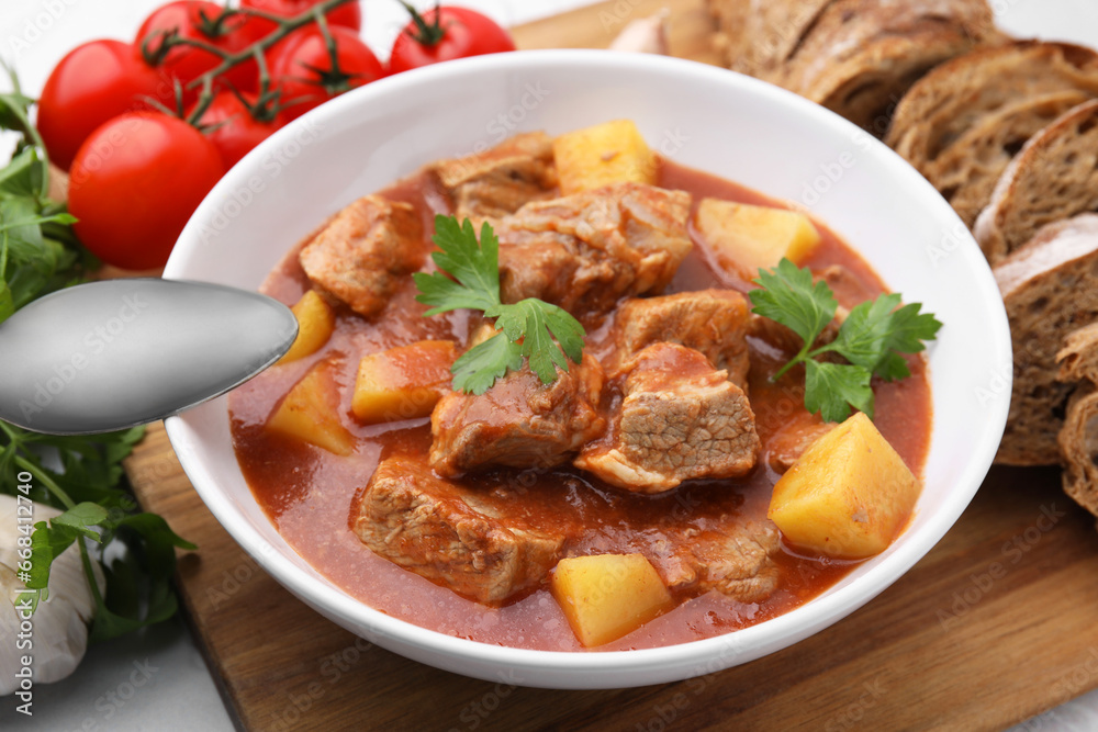 Delicious goulash in bowl, bread and ingredients on white table, closeup Delicious goulash in bowl, bread and ingredients on white table, closeup