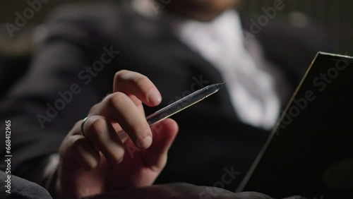 Close-up of a BUSINESSMAN twirling a pen and thinking. Holding a tablet for notes in the other hand, seated in office setting.