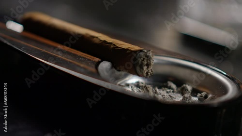 Close-up of a luxury cigar resting in a shiny ashtray. Dramatic lighting and shallow depth create an elegant, moody atmosphere.