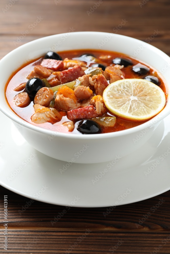 Meat solyanka soup with sausages, olives and vegetables on wooden table, closeup Meat solyanka soup with sausages, olives and vegetables on wooden table, closeup