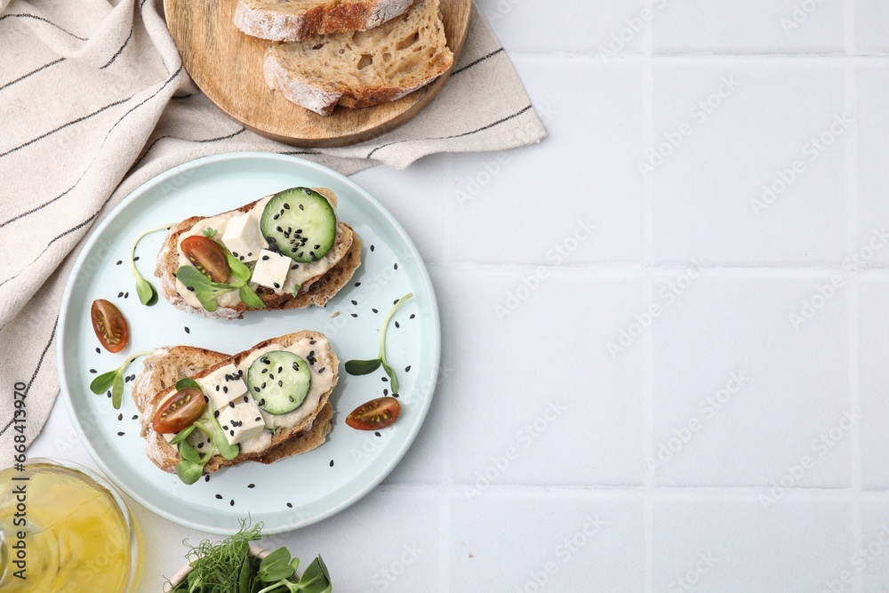 Tasty vegan sandwiches with tofu, cucumber, tomato and sesame seeds on white tiled table, flat lay. Space for text