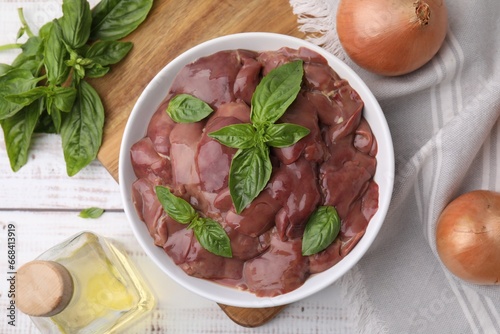 Bowl with raw chicken liver, basil and onions on white wooden table, flat lay