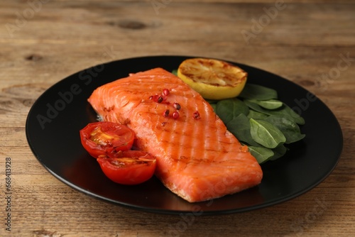 Tasty grilled salmon with tomatoes, lemon and basil on wooden table, closeup