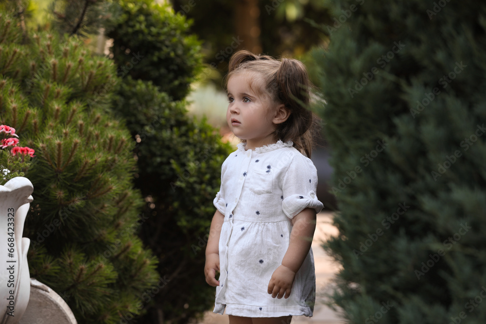 Cute little girl walking near green plants in park Cute little girl walking near green plants in park