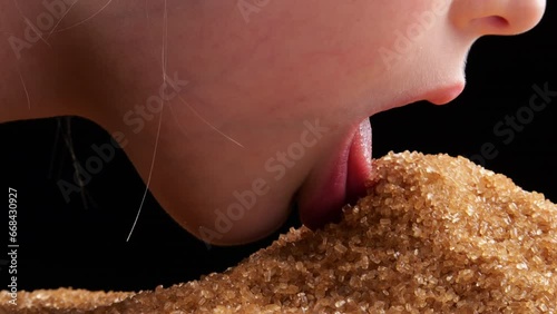 A GIRL touches a pile of brown SUGAR with her tongue, exploring its texture and sweetness in close-up view.