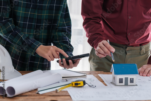 A group of engineers and architects are discussing the structure of a house building inside an office conference room.