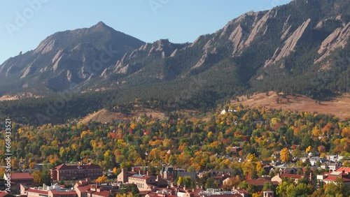 Aerial up close view of Flatiron mountains in Boulder Colorado surrounded by peak fall colors of green, red, and yellow trees showing the town and CU Boulder campus photo