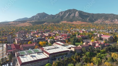 Aerial view of CU Boulder campus and Folsom football field surrounded by green and yellow fall trees with the rocky flatiron mountains in the background in the front range of Colorado panning left photo