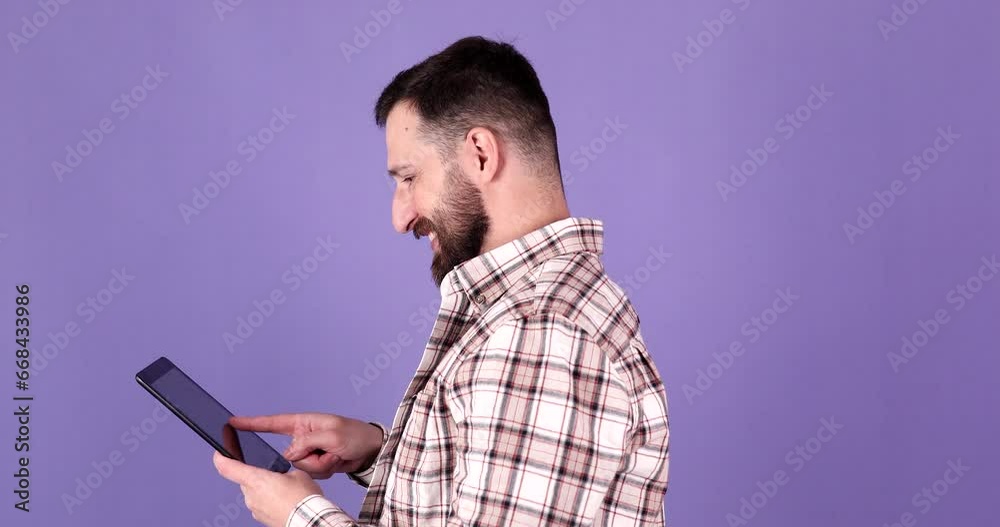 Young bearded man using digital tablet on purple background. Young bearded man using digital tablet on purple background.