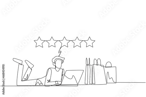 Continuous one line drawing young smiling man on stomach while typing on laptop. Next to the laptop is a shopping bag. Give the best review with pleasure. Single line draw design vector illustration