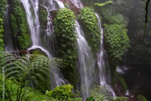 Beautiful waterfall in the jungle of southeast asia. A stream of water falls from high cliffs  breaking into streams  creating fog. High humidity in the tropical forest of Bali.