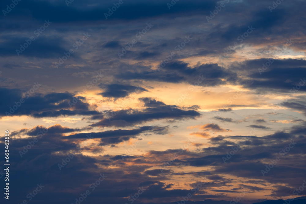 Sunset sky with golden rays of the sun against the background of silhouettes of mountain landscapes and rural villages. Aerial view of beautiful sky with clouds and sunlight during sunset.